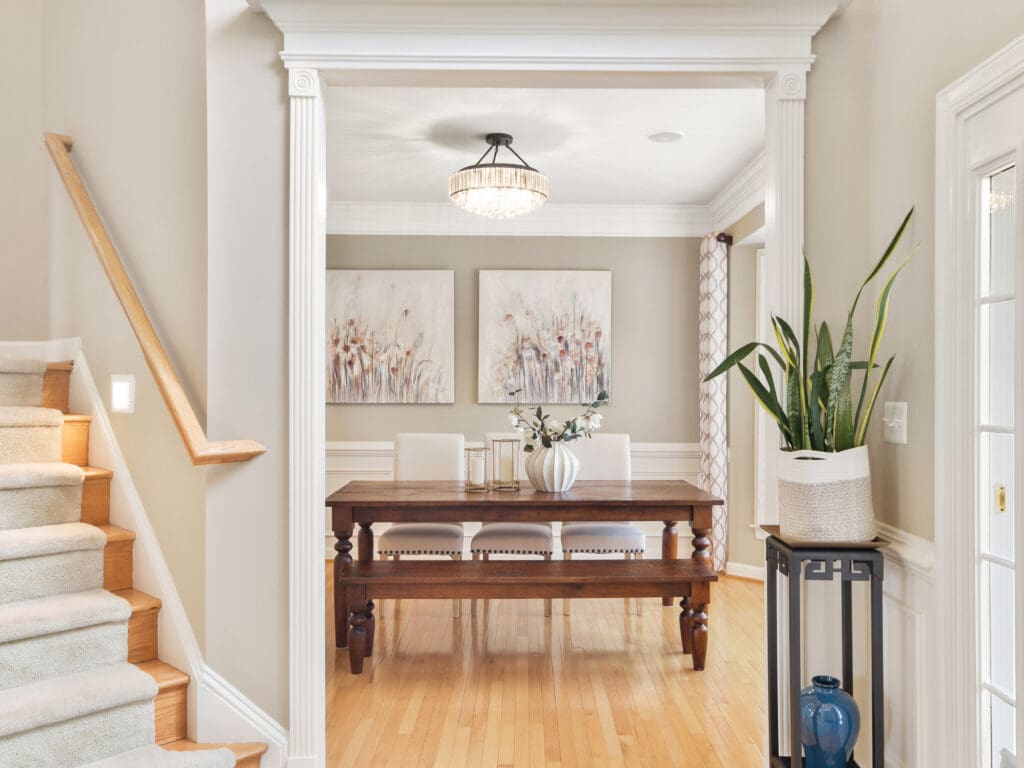 Stylish formal dining room with wood table, modern artwork, white trim, and decorative columns, professionally staged for home listing