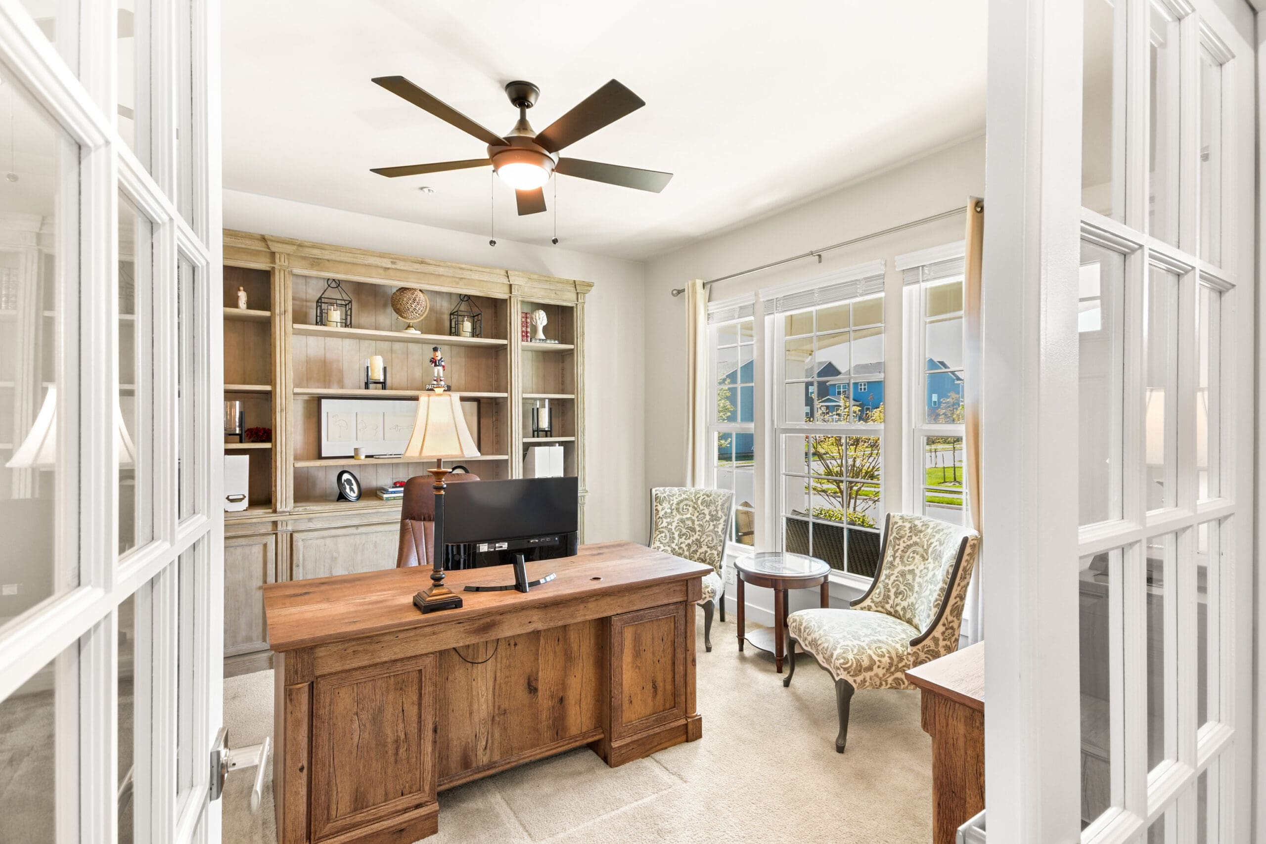 Home office featuring traditional wood desk, built-in shelving, French doors, and large windows with natural light for real estate photography