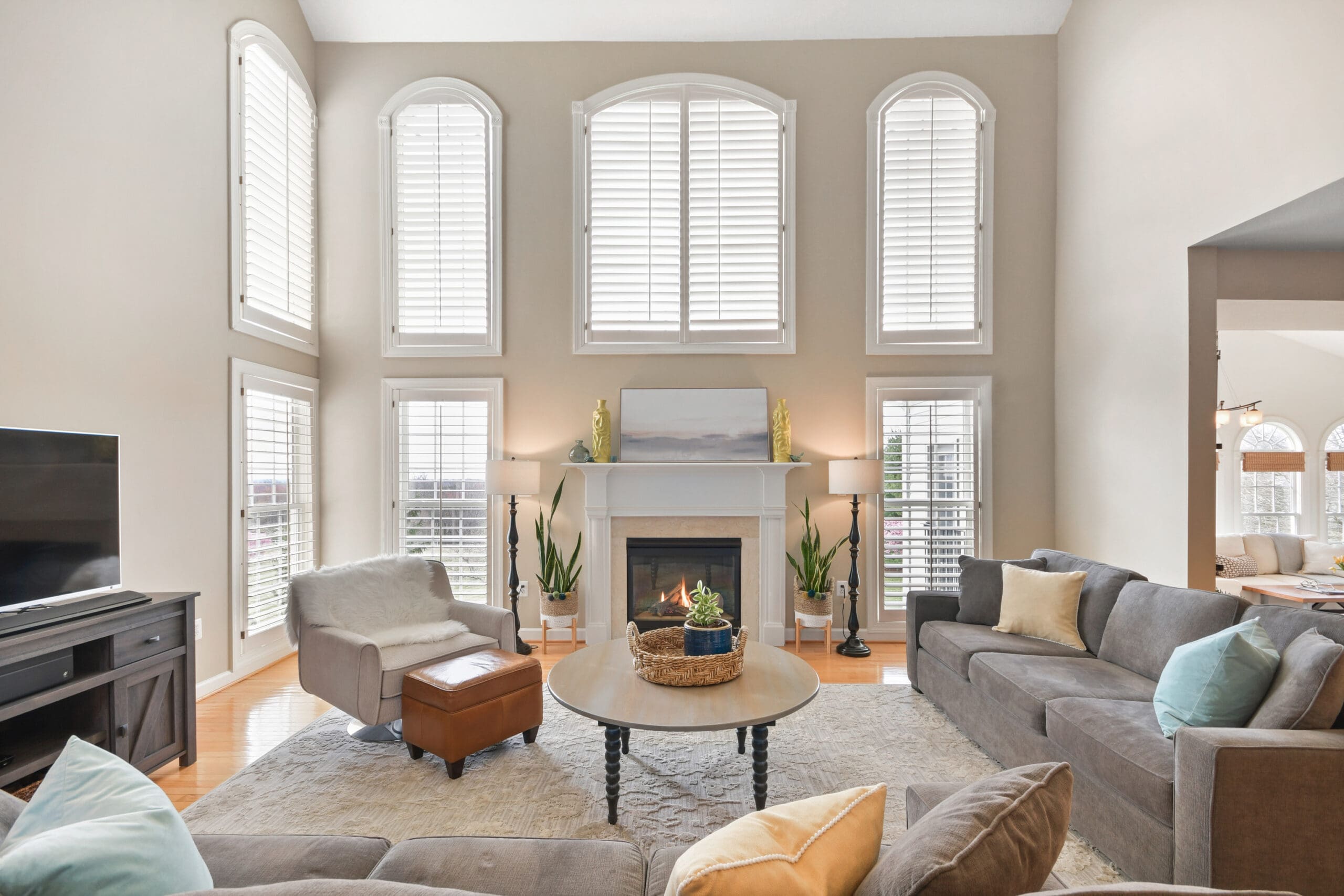 Grand two-story living room with floor-to-ceiling windows, fireplace, gray sectional sofa, and neutral decor staged for luxury home listing