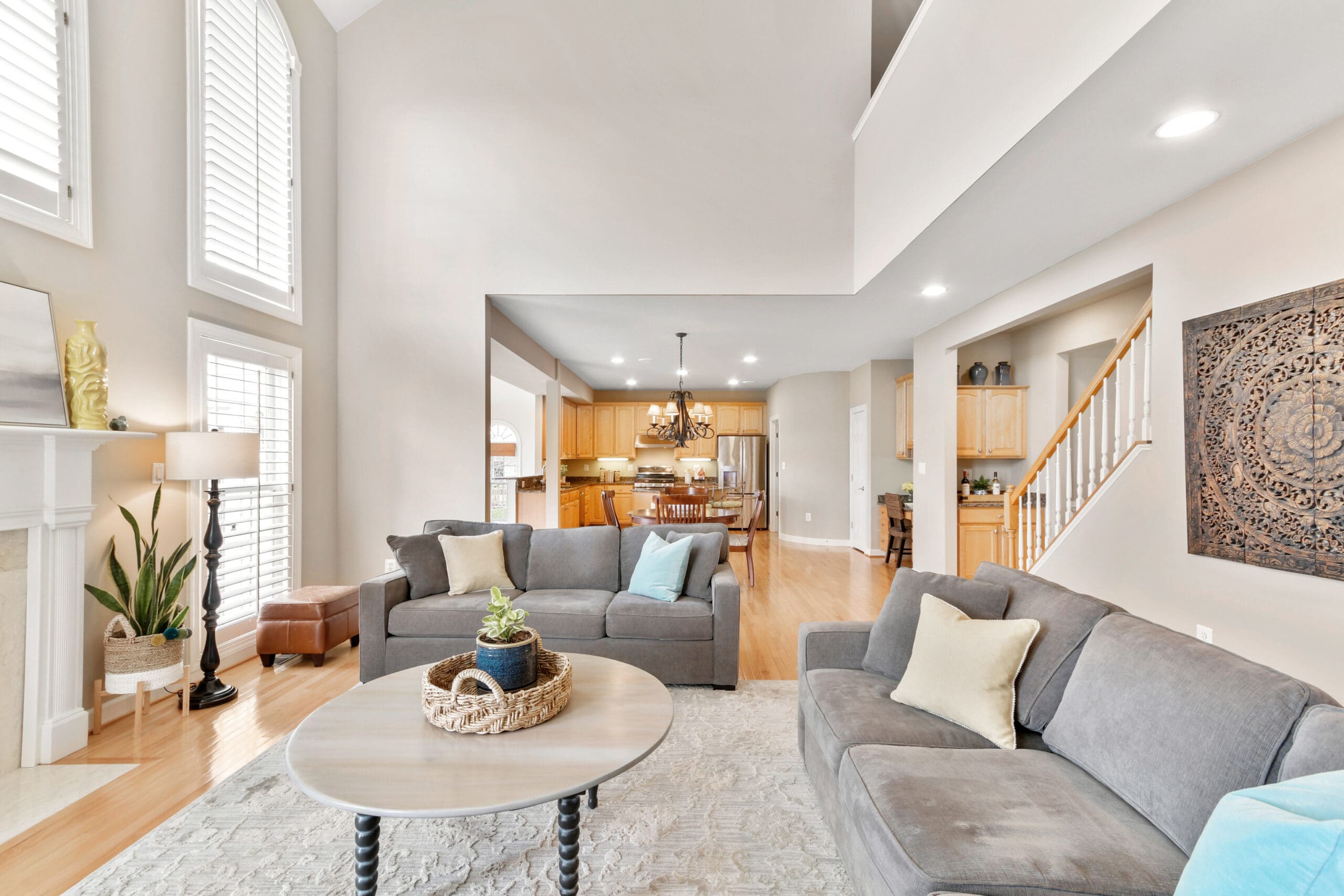Inviting family room with dual gray sofas, round coffee table, fireplace, and view into spacious kitchen and staircase, staged for real estate photography
