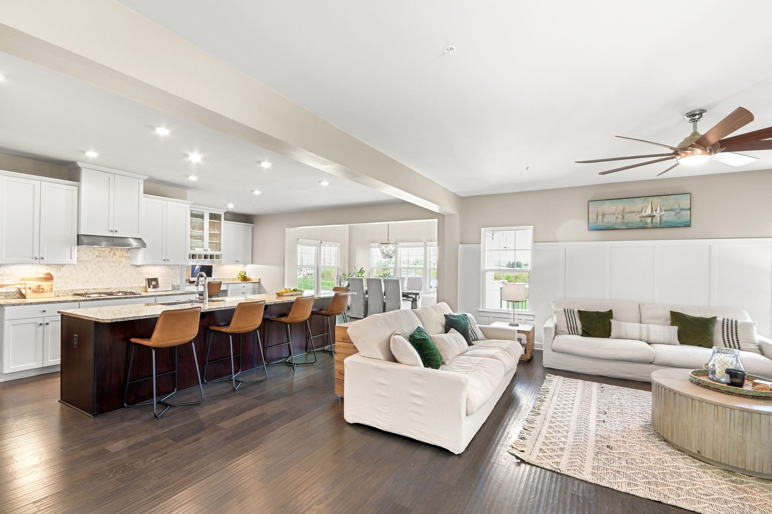 Open-concept kitchen and living room with white cabinetry, dark wood island, leather bar stools, and modern coastal decor, professionally staged