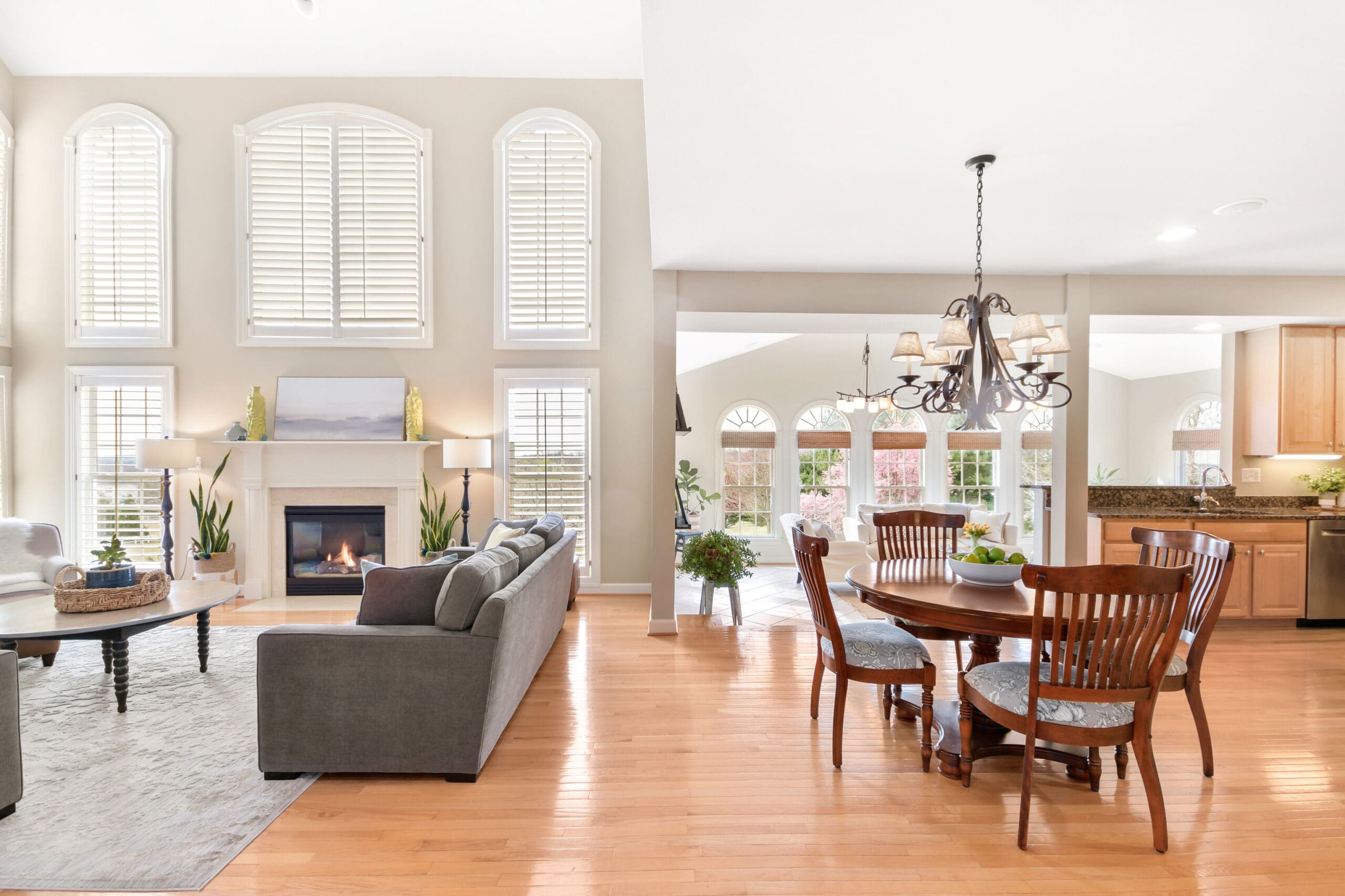 Elegant great room with high ceilings, arched windows, fireplace, gray sectional sofa, and round dining table in an open floor plan